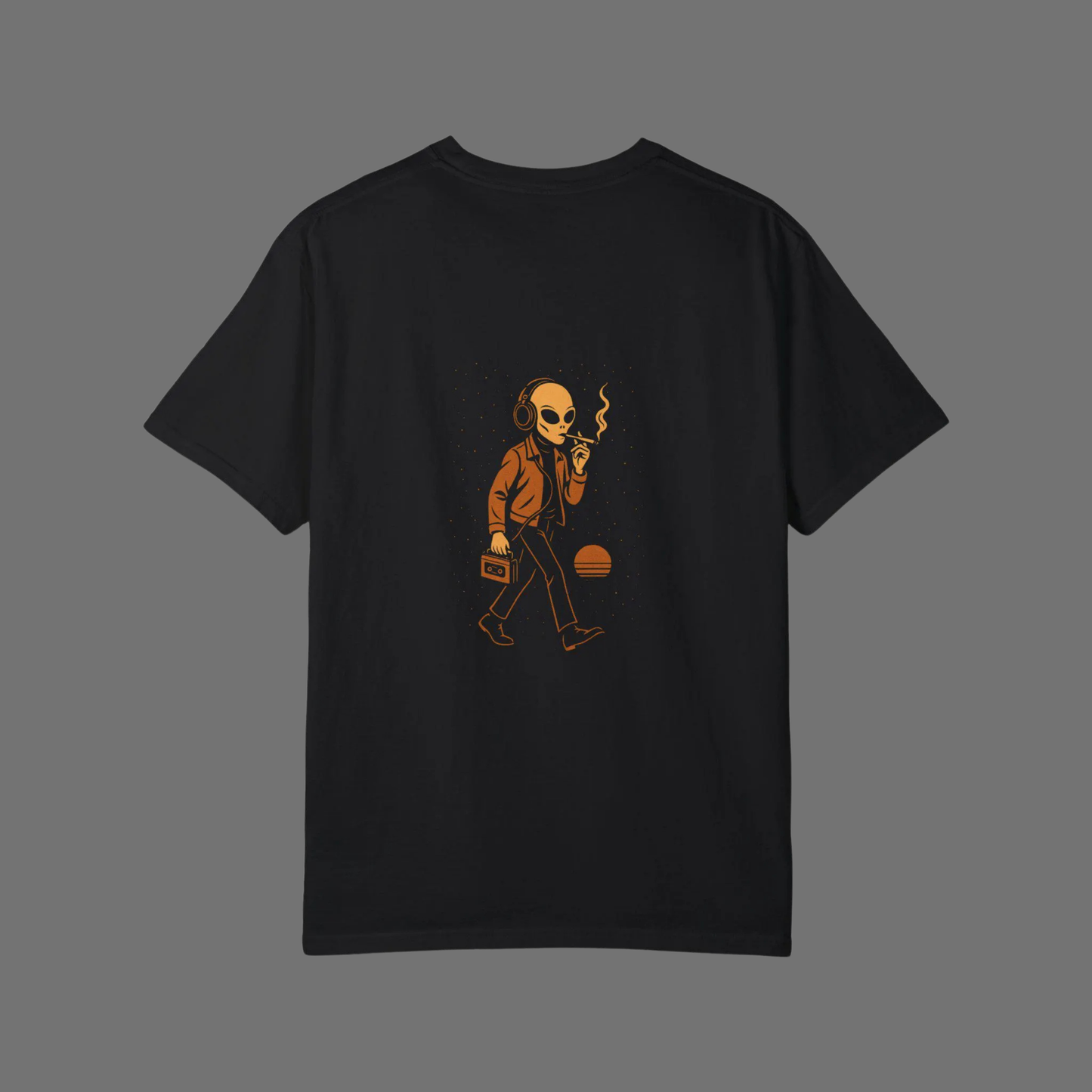 Flat lay of black oversized t-shirt with orange graphic print of a smoking alien wearing headphones and holding a cassette player, displayed on a neutral gray background.
