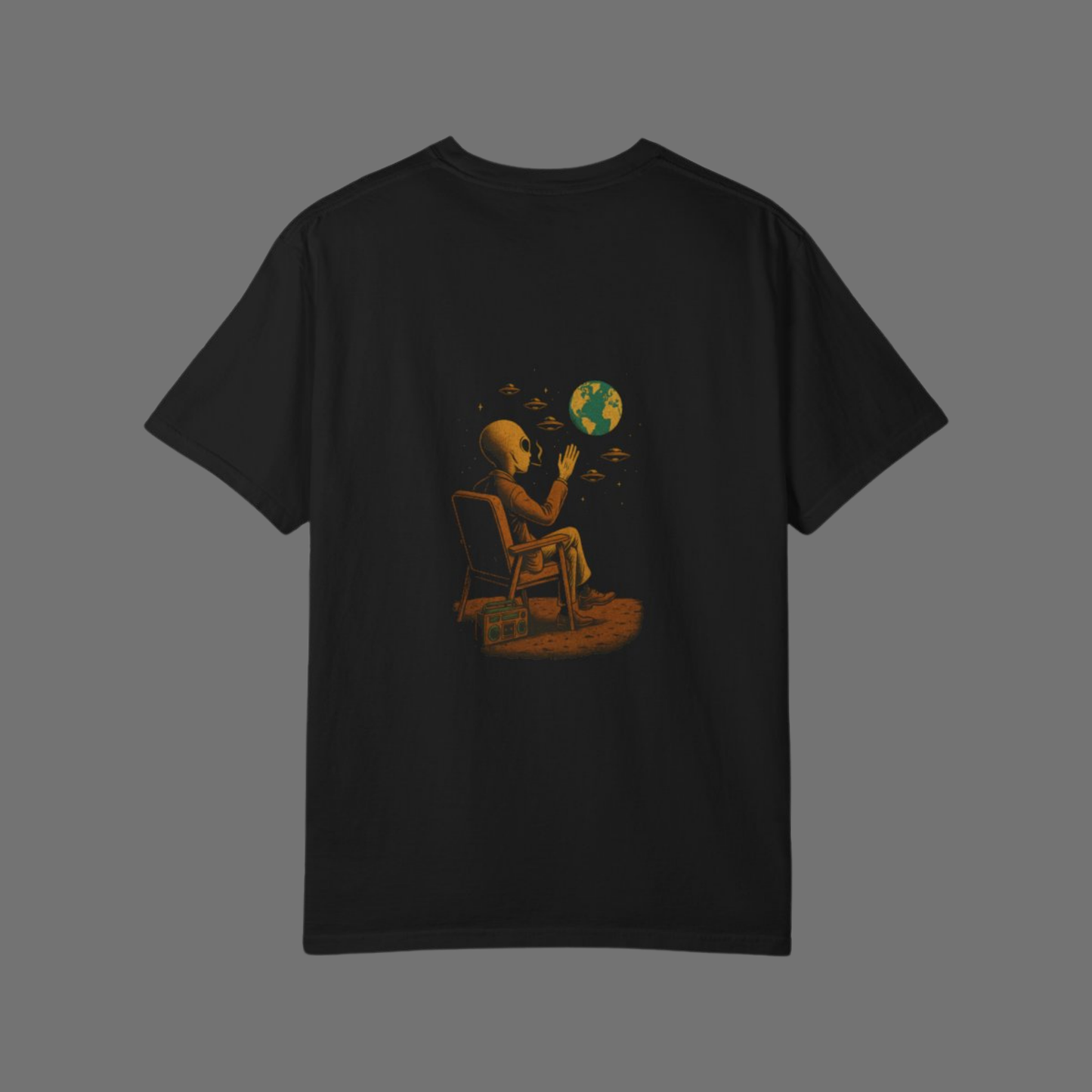 Flat lay of a black Comfort Colors 1717 t-shirt featuring a back print of an alien sitting on a chair, waving at Earth, with flying saucers in the sky.