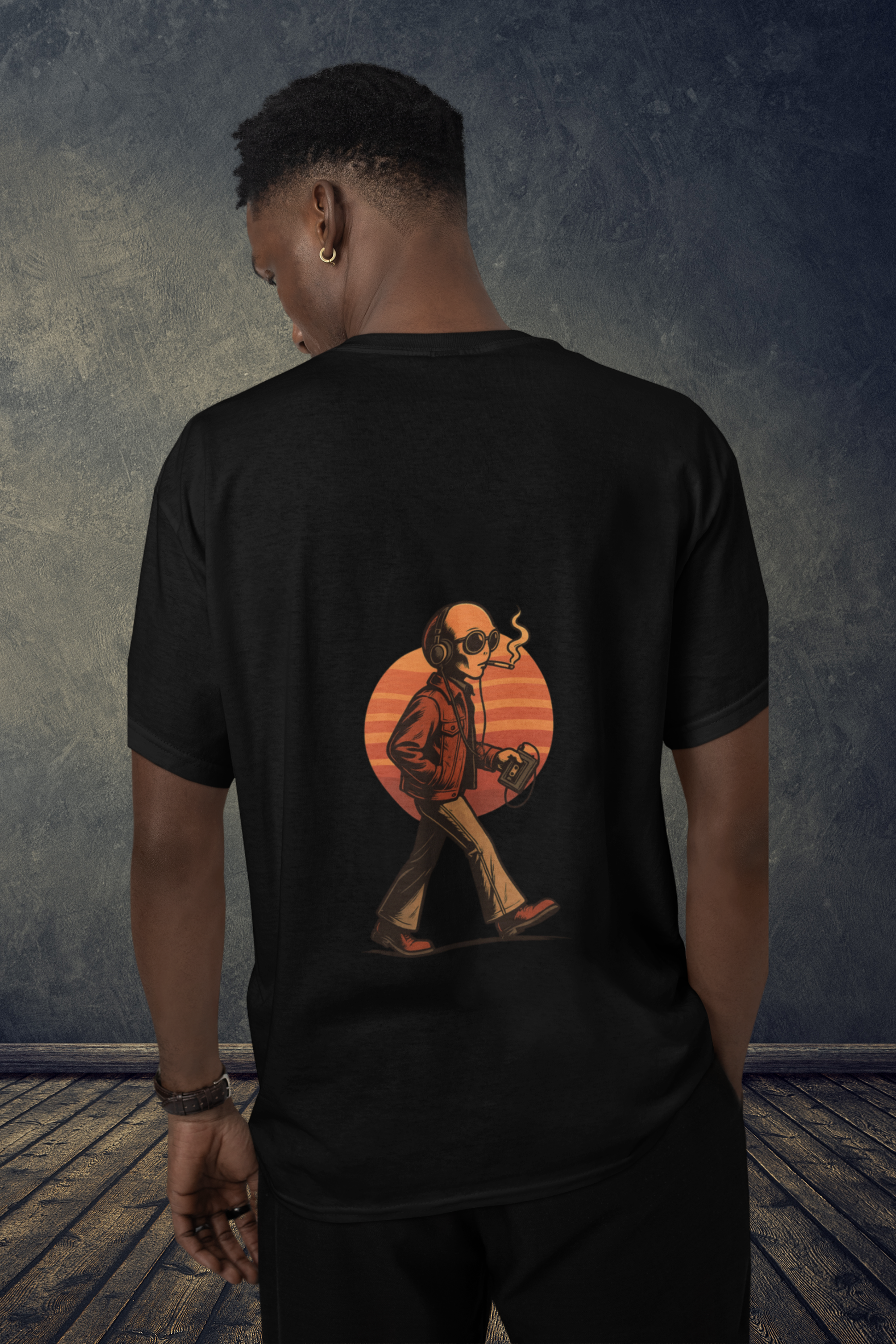 Man wearing a black oversized t-shirt with back-printed alien graphic in front of a textured wall background
