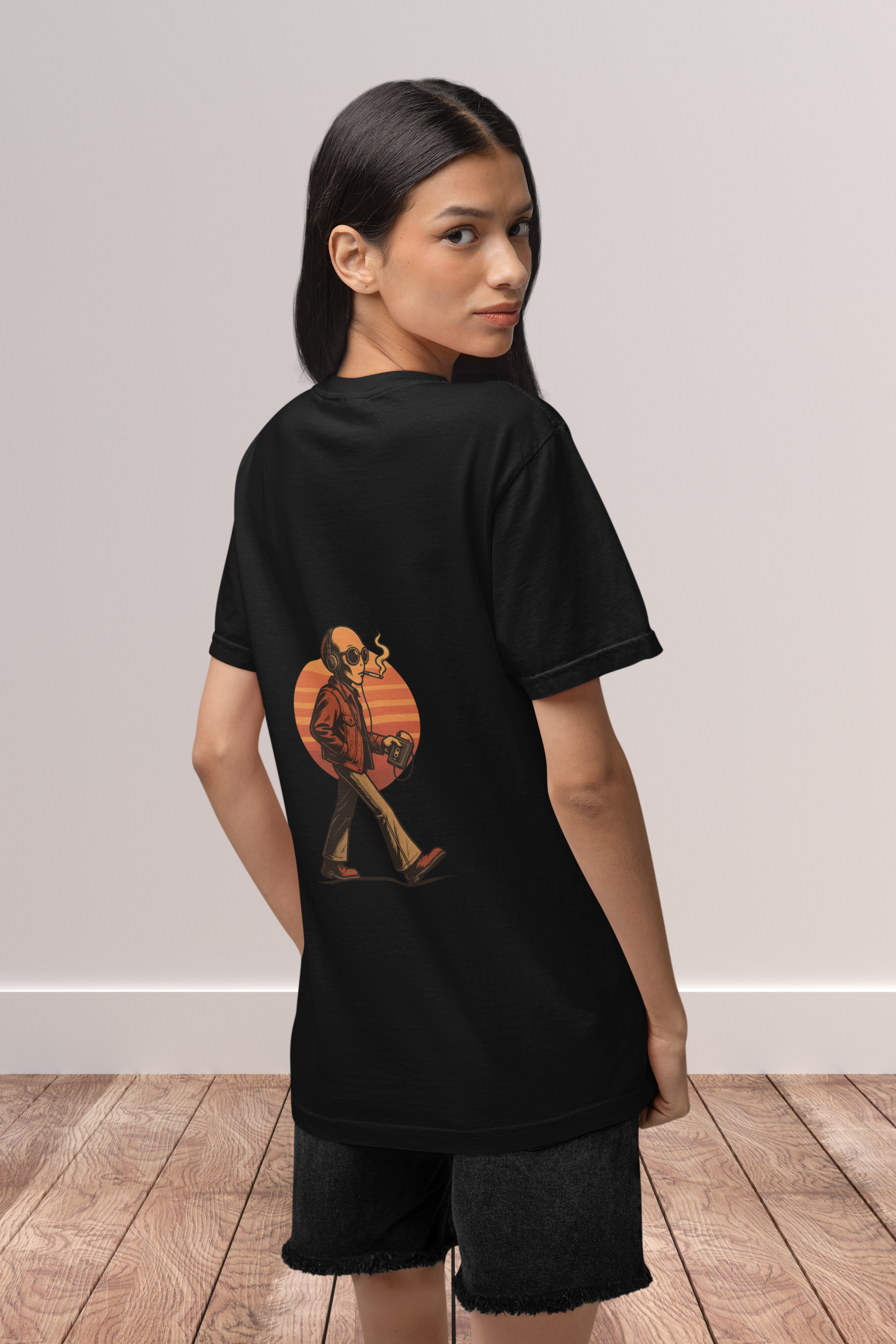 Woman wearing oversized black t-shirt with back print of retro alien smoking and walking under sunset