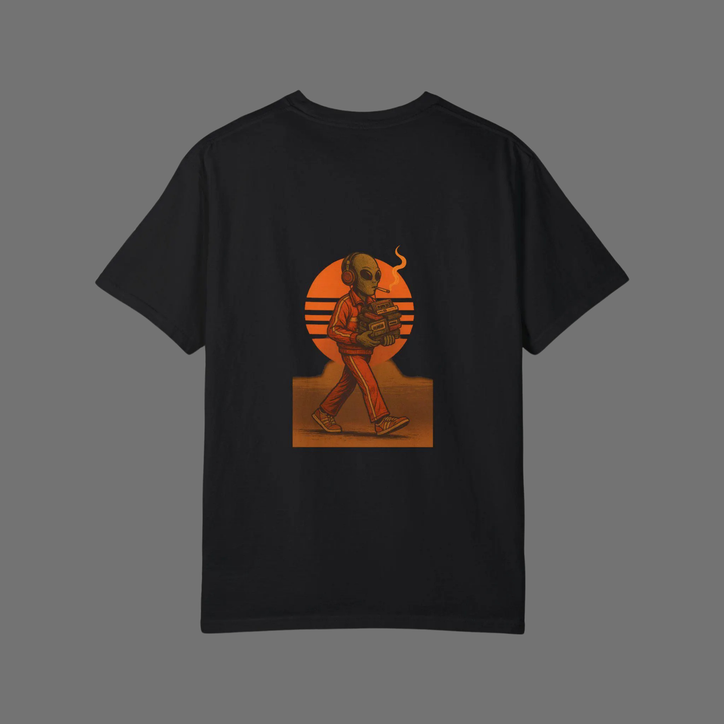 Flat lay of a black oversized t-shirt on gray background, featuring a bold back print of a retro-styled alien smoking and holding a cassette player, set against an orange sunset graphic.