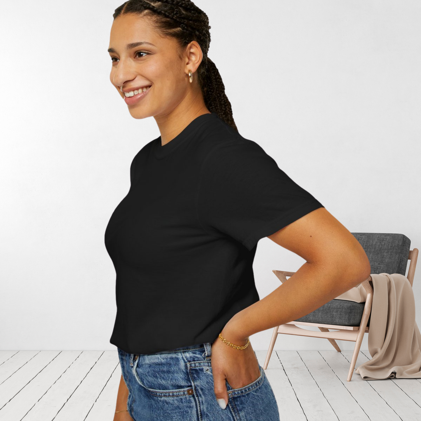 Smiling woman in a plain black oversized t-shirt, posing in a cozy minimalist room with light wood flooring and a gray chair in the background.